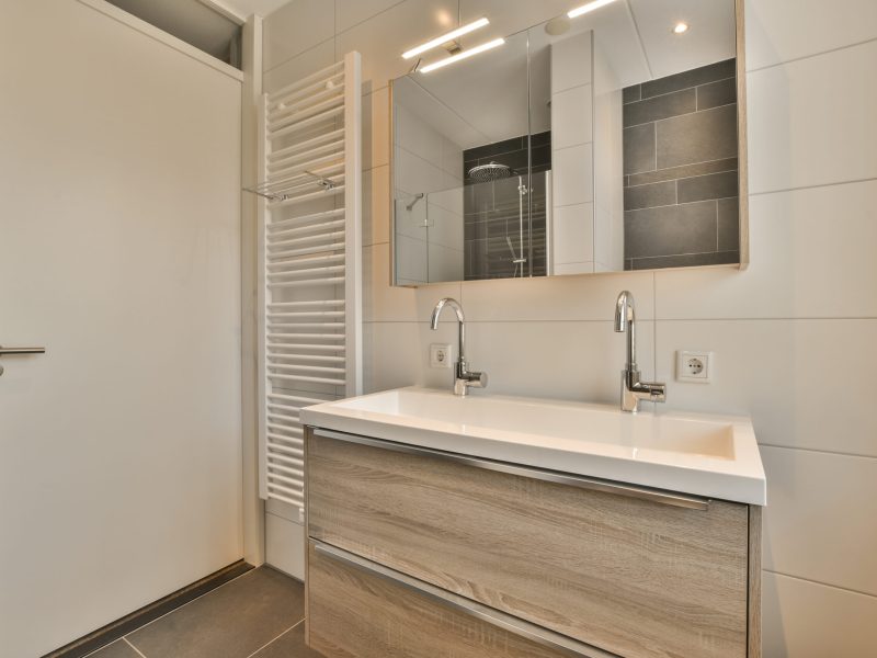 a modern bathroom with white walls and wood flooring, along with a wall mounted mirror above the sink area