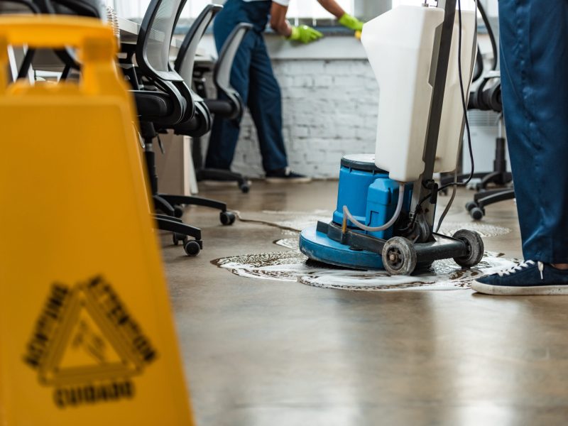 cropped view of cleaner washing floor with cleaning machine near colleague