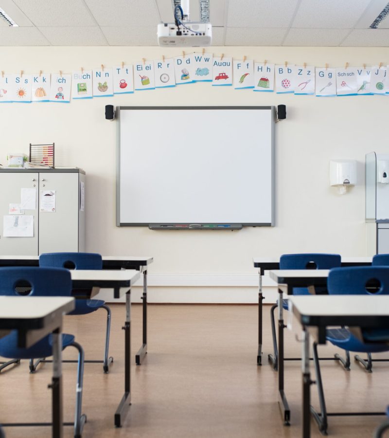 School desk and chairs in empty modern classroom. Empty class room with white board and projector in elementary school. Primary classroom with smartboard and alphabet on wall.