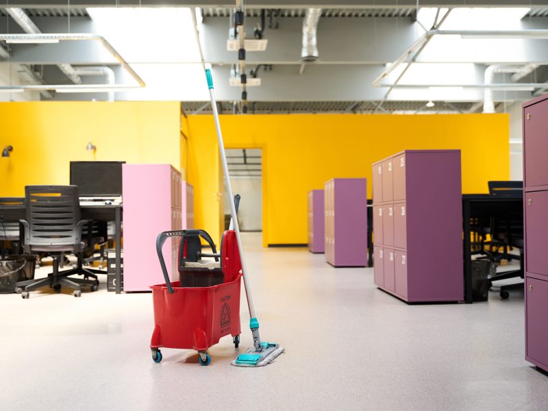 Red cleaner cart with work gadgets and mop stand in the middle of an office area in a coworking space